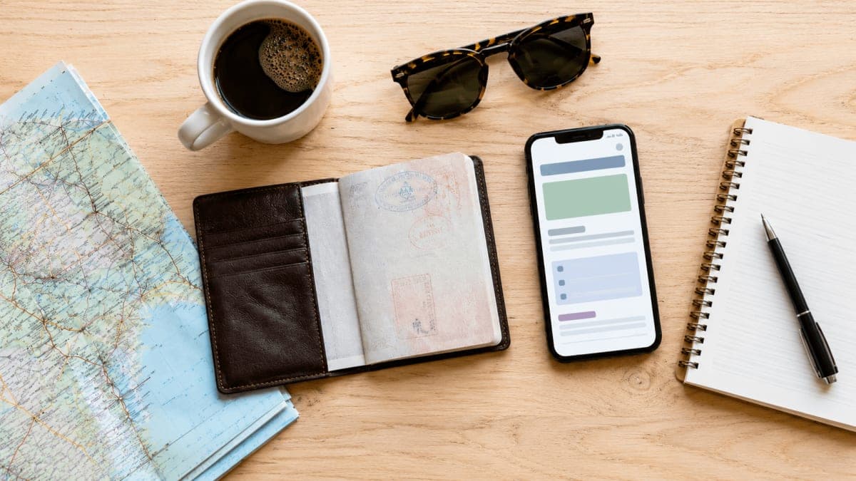 Overhead flat-lay of trip planning — map, passport, phone with a clean itinerary, and coffee on a table
