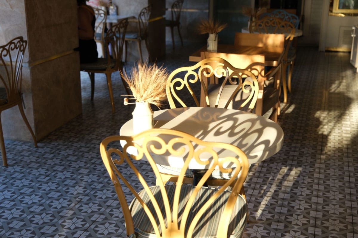 A quiet sunlit cafe corner with wrought iron chairs and patterned tiled flooring